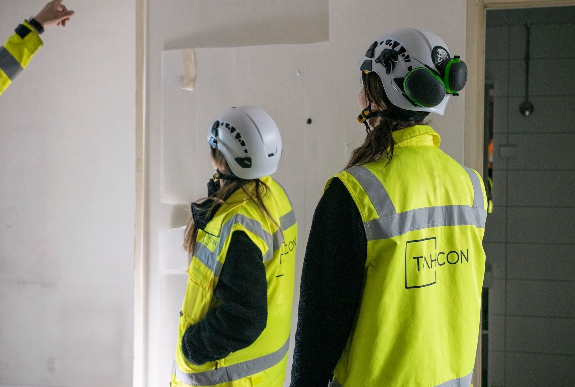 Huomioliiveihin pukeutuneet rakennusalan työntekijät tarkastelevat seinää remonttikohteessa