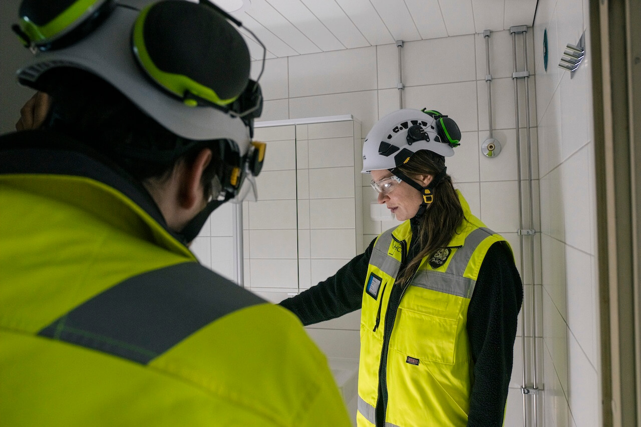 Kaksi huomioliiviin ja valkoiseen kypärään pukeutunutta työmaahenkilöä tarkastaa kylpyhuonetta.